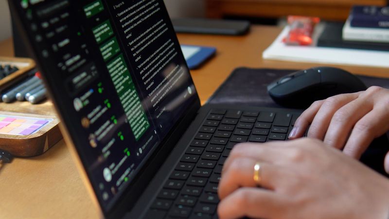 Mãos digitando no notebook, com uma lista de conversas aberta na tela