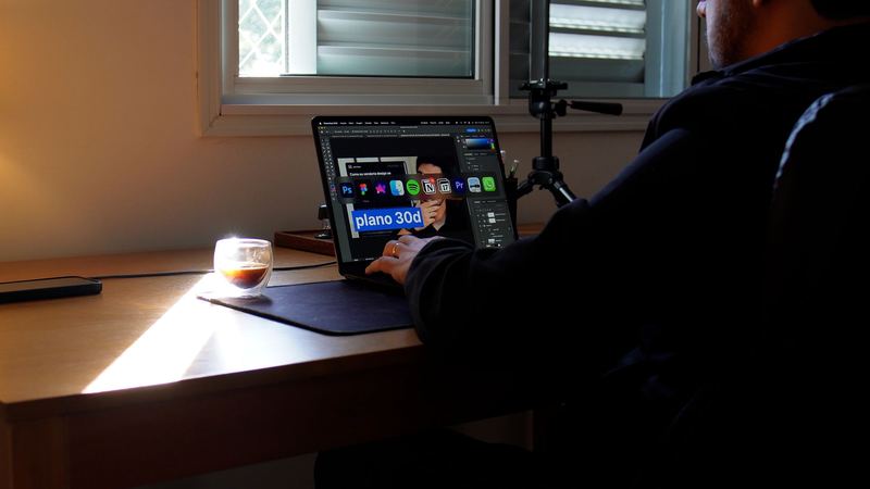 João trabalhando no notebook, na mesa do escritório, com a luz da tarde